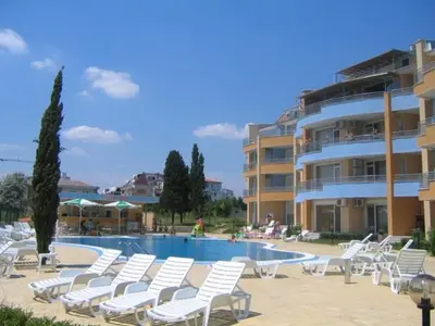 a swimming pool with white chairs and a building at Apartments Lucky Complex Ravda in Ravda