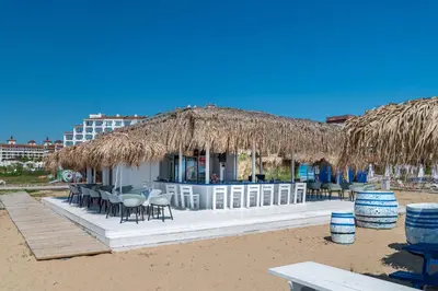 a restaurant on the beach with chairs and a straw roof at Sunrise All Suites Resort- All Inclusive in Obzor
