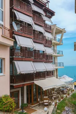 a tall building with tables and umbrellas next to the ocean at Fjord B&B in Sozopol