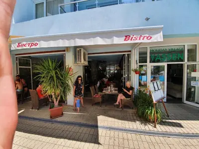 a woman standing outside of a shop with people sitting outside at Yassen Holiday Village in Sunny Beach