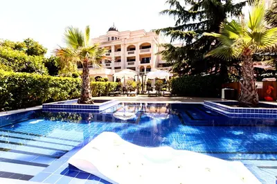 a swimming pool with palm trees and a building at Primoretz Grand Hotel & Spa in Burgas City