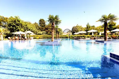 a large swimming pool with palm trees and umbrellas at Primoretz Grand Hotel & Spa in Burgas City