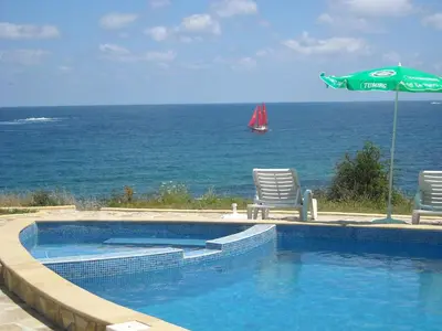 a swimming pool with two chairs and an umbrella and the ocean at Aparthotel Romance in Kiten