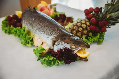 a fish on a plate with fruits and vegetables at Hotel Wela - Premium All Inclusive in Sunny Beach
