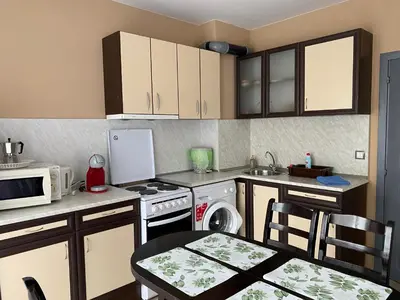 a kitchen with white cabinets and a table and a microwave at Belchevi Apartments in Burgas City