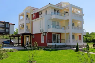 a white and red building with a green yard at St. Stefan Villas & Hotel in Sozopol