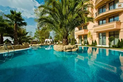 a large swimming pool with a palm tree in front of a building at Aphrodite Rose Apartment in Sunny Beach
