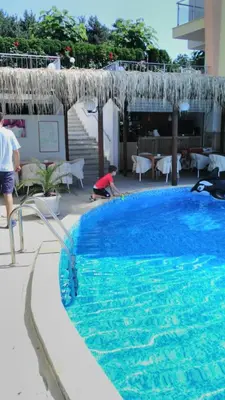 a person is sitting next to a swimming pool at Alex Beach Apartment in Sveti Vlas