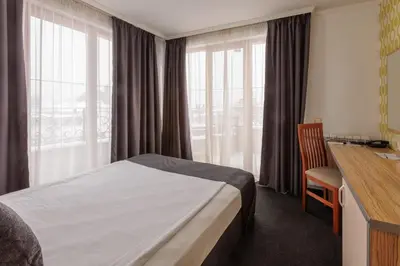 a hotel room with a bed and a desk and window at Семеен Хотел Опера in Burgas City