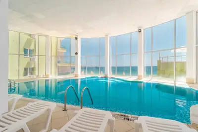 a large swimming pool with white chairs and windows at MPM Hotel Arsena - Ultra All Inclusive in Nesebar