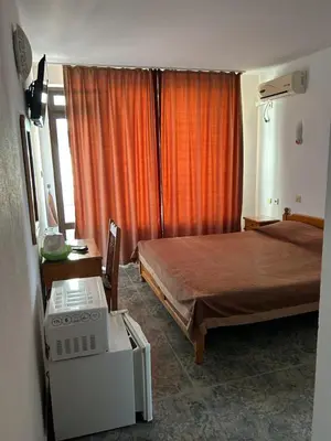 a bedroom with a bed and a window with an orange curtain at КЪЩА