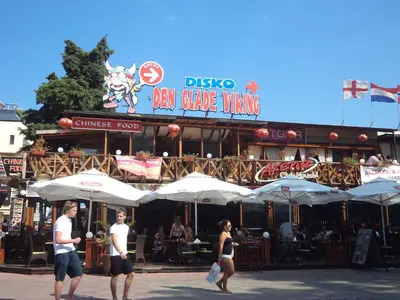 two people walking in front of a bar with umbrellas at Family Hotel Romantik in Sunny Beach