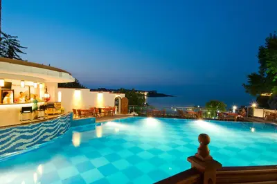 a swimming pool with a view of the ocean at night at Hotel Villa List in Sozopol