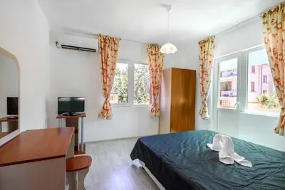 a bedroom with a bed and a desk and two windows at Guest House Galema in Obzor