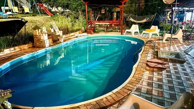 a swimming pool in a backyard with a patio with chairs and a swing at Guest House Evin Rai in Byala