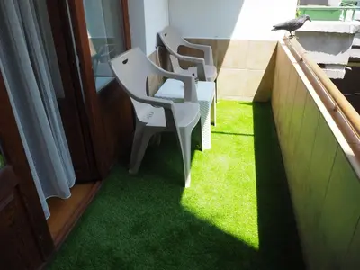 a balcony with three chairs and a bird sitting on the grass at Yoana Apartment in Varna City