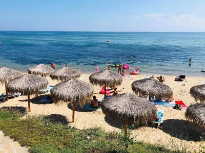 a beach with straw umbrellas and people in the water at PS Apartment / SunCoast Resort in Sveti Vlas