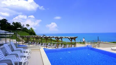 a swimming pool with white chairs and the ocean at Апартаменти Бяла Клиф на плажа - Apartments Byala Cliff First Line in Byala