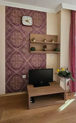 a living room with a tv and a clock on a wall at Excelsior Holiday Apartments Sunny Beach in Sunny Beach