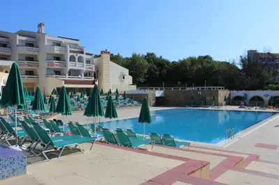 a swimming pool with lawn chairs and umbrellas at Duni Pelican Hotel - All Inclusive in Sozopol