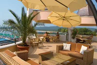a balcony with chairs and tables and umbrellas at Duni Marina Beach Hotel - All Inclusive in Sozopol