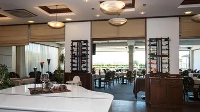 a dining room with tables and chairs and a room with windows at Long Beach Resort in Shkorpilovtsi