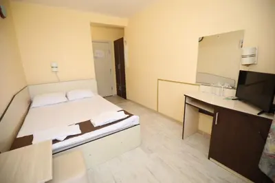 a room with a bed and a desk and a television at Family Hotel White House in Pomorie