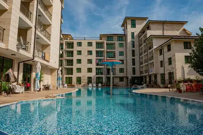 a swimming pool with an umbrella in front of some buildings at Amadeus Lux - Menada Apartments in Sunny Beach