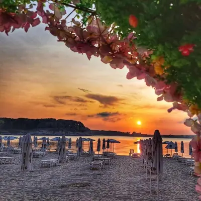 a beach with chairs and umbrellas at sunset at Guest House Kostovi in Kiten
