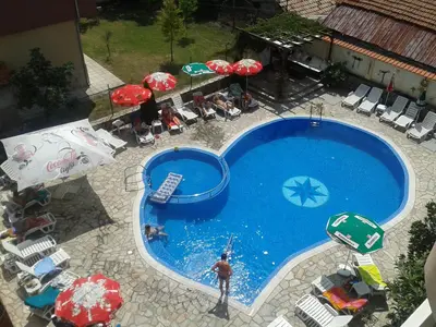 a man is standing next to a swimming pool with umbrellas at Saint George Family Hotel in Lozenets