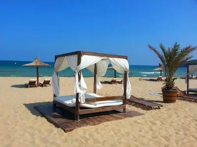 a bed on a beach with umbrellas and the ocean at Menada Sozopol Apartments in Sozopol
