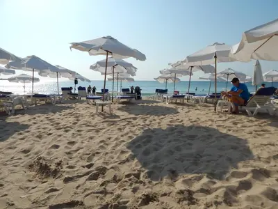 a beach with umbrellas and people sitting on the sand at Dunav Apt.1 in Ravda