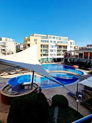 a large pool with a white umbrella next to a building at Pool View Studio, Pollo Resort, Sunny Beach in Sunny Beach