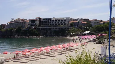 a beach with pink and white umbrellas and the water at Sozopoli Hills Simeonov Apartments in Sozopol