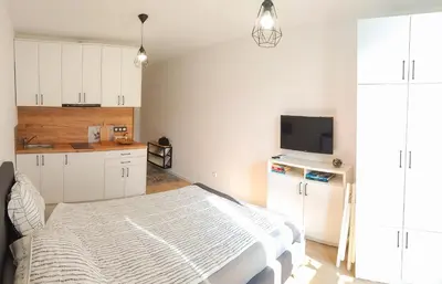 a white bedroom with a bed and a tv at Loli’s Beach Studio in Burgas City