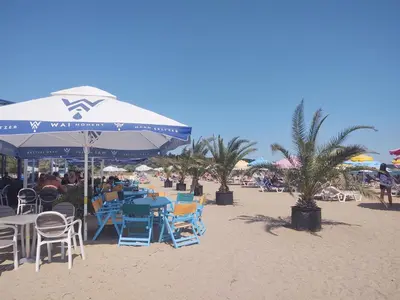 a beach with tables and chairs and an umbrella on the sand at Loli’s Beach Studio in Burgas City