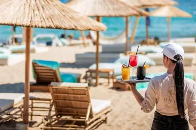 a woman holding a tray with drinks on the beach at Onyx Beach Residence - Free Beach Access & Parking in Sveti Vlas