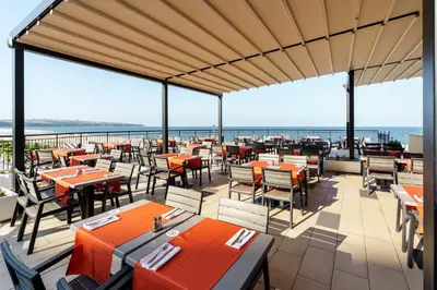 a restaurant with tables and chairs and the ocean at Alua Helios Bay - All Inclusive in Obzor