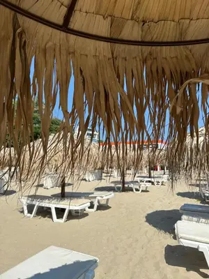 a straw umbrella on a beach with chairs and tables at Аппартамент в Триумфе Святой Влас 300м от моря, бассейн. in Sveti Vlas