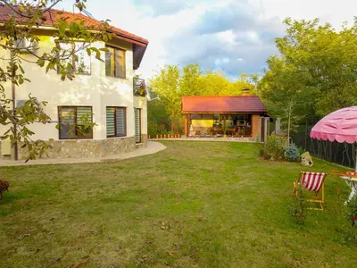 a yard with a house and a house with a pink umbrella at Къща за гости АКАЦИЯ in Ravna Gora