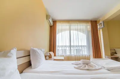 a hotel room with a white bed with a window at ТРОПИКАНА in Primorsko