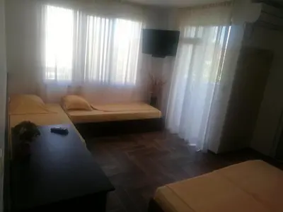 a room with two beds and a table and curtains at Къща за гости ЕЛИ in Primorsko