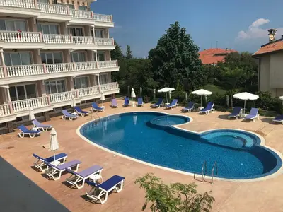 a swimming pool in front of a hotel with chairs and umbrellas at Студио Сънрайз А28, Лозенец in Lozenets