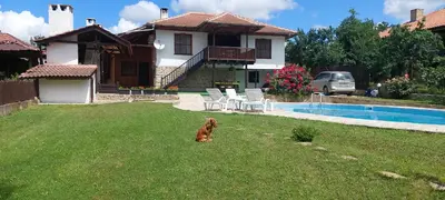 a dog sitting in the grass in front of a house at СЪНТОВЕЦ - на брега на язовир Цонево in Tschenge