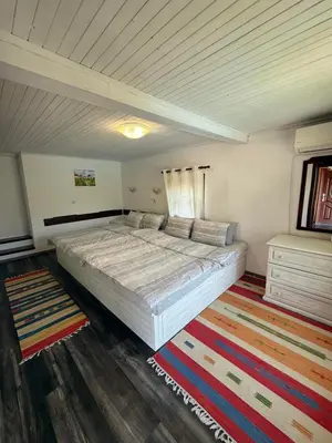 a bedroom with a large white bed and a rug at СЪНТОВЕЦ - на брега на язовир Цонево in Tschenge