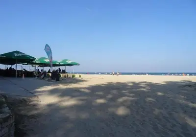 a beach with green umbrellas and people sitting on the beach at CarolMike Oasis Beach Apartment Kamchia Reserve in Kamchia