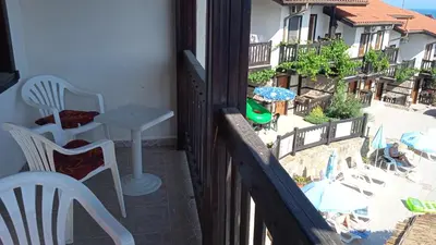 a balcony with white chairs and a table and a building at Pearl Apartments Sozopol in Sozopol