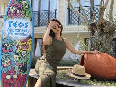 a woman sitting on a bench next to a surfboard at Teos Apartments Primorsko in Primorsko