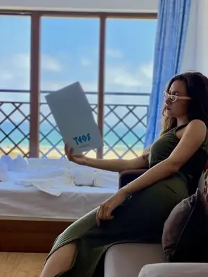 a woman sitting on a bed reading a book at Teos Apartments Primorsko in Primorsko