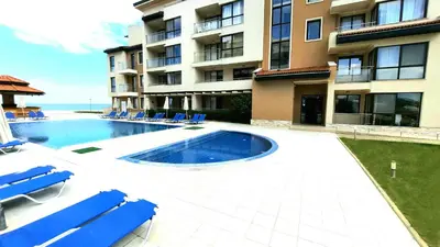 a swimming pool next to a building with blue chairs at Obzor Beach Resort Apartment G-109 in Obzor